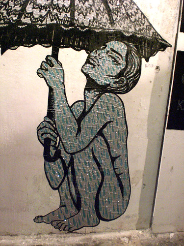 street art of a nude woman, folded into a tight crouch, looking up and holding an umbrella above her