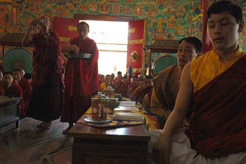 Monk taking the photo opportunity during a mandala offering, senior lamas of the Sakya school, tea cups, drum, pink and gray marble, short tables, traditional robes, Lamdre, Tharlam Monastery of Tibetan Buddhism, Boudha, Kathmandu, Nepal by Wonderlane