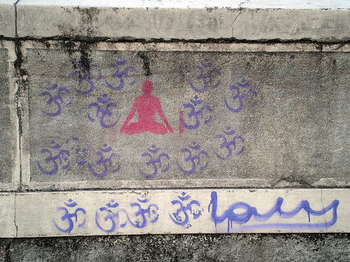 stencil graffiti of a pink person sitting in lotus position surrounded by blue oms