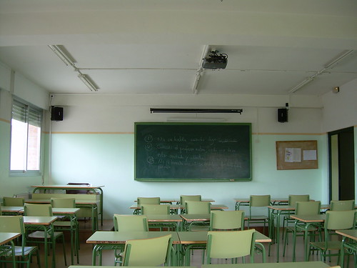 Un aula con pupitres verdes. Al fondo, la pizarra.