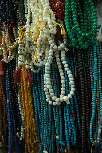 Blue, green, gold, and white, bone mala beads, head beads, guru beads, mala makers and sellers, at the wish fulfilling Great Stupa. Boudha, Kathmandu, Nepal by Wonderlane