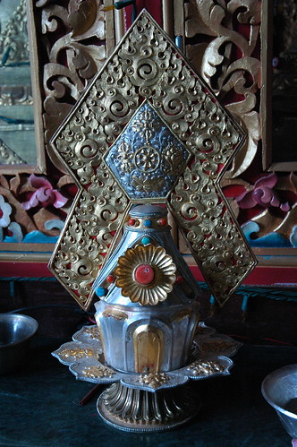 Ornately worked silver, coral, turquoise ritual torma offering on lotus dish with 8 auspicious symbols, flames of wisdom, Sakya Monastery, Tibetan Buddhism, wood frame in background, Pharping, Nepal by Wonderlane