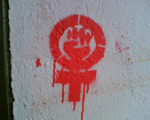 A graffiti in red ink on a white wall of the feminist power fist.
