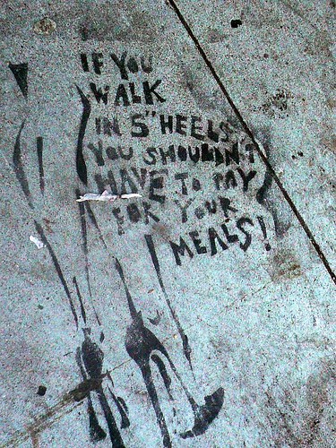 graffiti of legs wearing tall heels, with the words, "if you wear 5" heels, you shouldn't have to pay for your meals!"