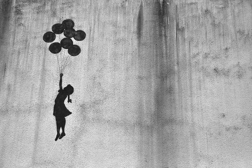 graffiti of a silhouette of a small girl holding a bunch of balloons, floating flying going