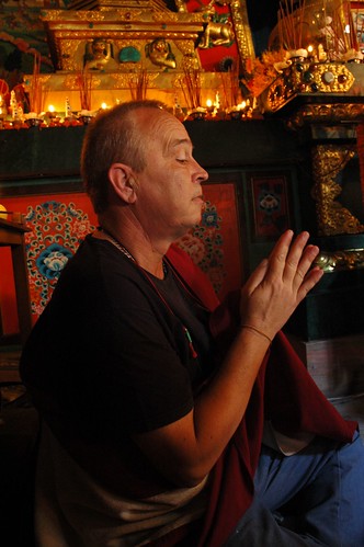 Steve D. at Sakya Lamdre, prays, offerings and shrine above his head, Tharlam Monastery of Tibetan Buddhism, Boudha, Kathmandu, Nepal by Wonderlane