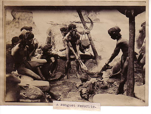 Tribesmen roast a dog over an open fire. At their feet is a severed human head -- perhaps they were celebrating a victory against an enemy tribe.   Philippine Buhay Pinoy Noon old pictures photograph black and white Philippines  Filipino Pilipino  people photos life Philippinen indigenous igorot    