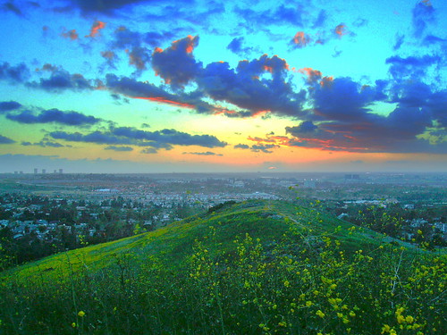Sunset behind a cloud over the Pacific Ocean from French Hill Turtle Rock Irvine California looking West , Newport Center highrise buildings to the left on the horizon, University of California at Irvine in the center midground. clouds blue orange green