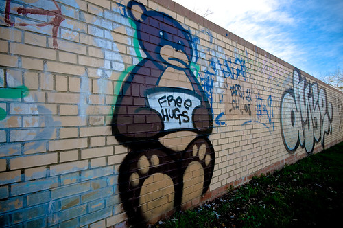 graffiti of big brown bear holding a sign: free hugs