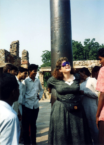Linda Lane putting her arms around the iron pole, backwards for luck, on pilgrimage, Old Delhi, India, in 1993 by Wonderlane