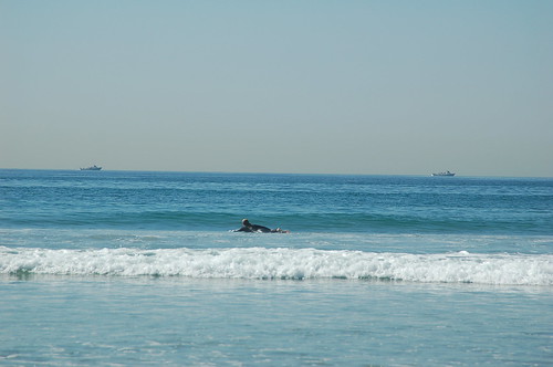 One surfer and two naval ships in the waters off San Diego