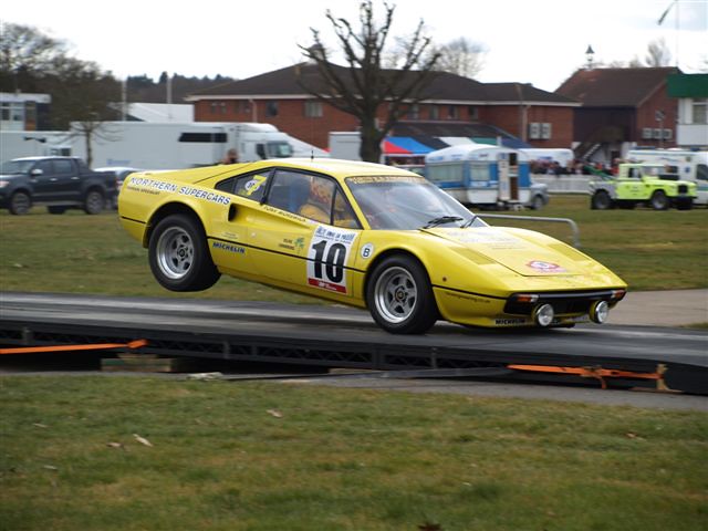 Yellow Ferrari 308GTB rally car landing from a jump