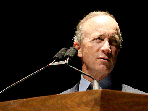 Mitch Daniels, a white man, stands at a podium. He is wearing a suit and tie.