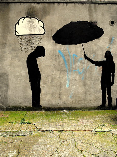 graffiti of silhouette standing beneath a raincloud, and another silhouette offering that person an umbrella