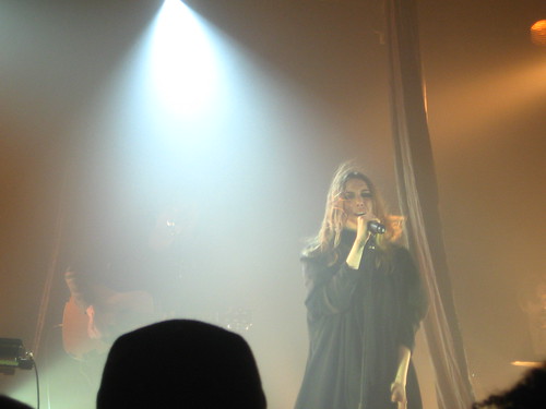 Lykke Li onstage, surrounded by fog and spotlights as she sings into a microphone and her dirty-blonde hair blows over her face.