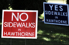 Signs for and against new sidewalks line the streets.