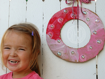 Child smiling standing next to a cardboard holiday wreath
