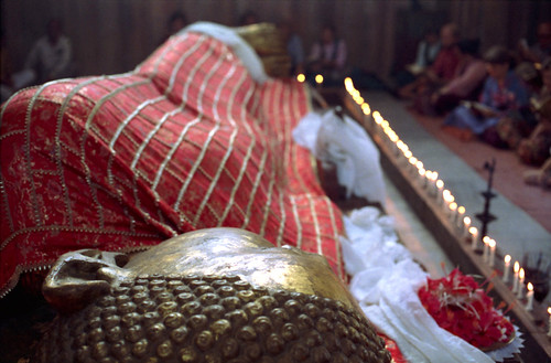 Statue where Lord Buddha died - Buddha's Parinirvana Statue, reclining Buddha, with offerings, katags, Buddhist practitioners, flower and candle offerings, Kusinara, India, pilgrimage, 1993 by Wonderlane
