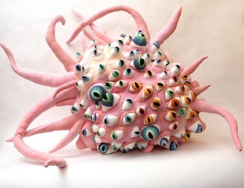 A large, roundish pale pink creature with long tentacles, also pink, extending in all directions. The creature is nearly covered with eyeballs with irises in all different colors, many of which are shades of green, blue or orange.