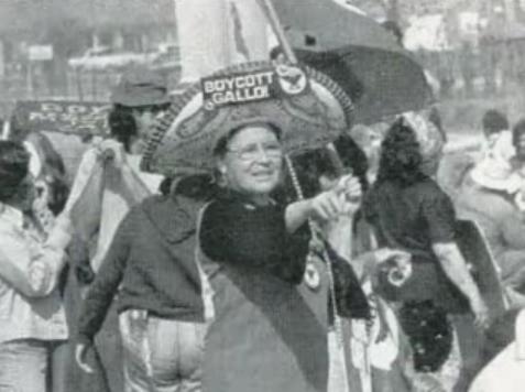An older De La Cruz at a protest. She is pointing and wearing a sombrero that reads 'Boycott-Gallo!'