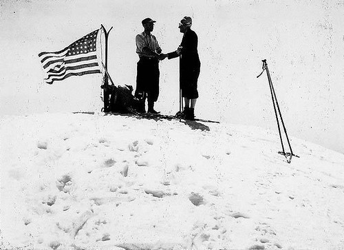 Two skiers atop the summit of Mt. Baker standing next to a U.S. flag