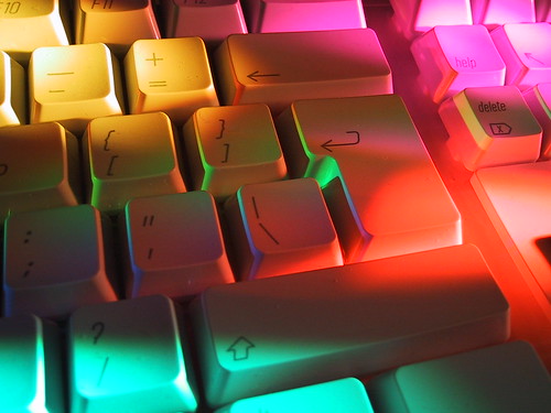 A computer keyboard with different coloured light shining on it
