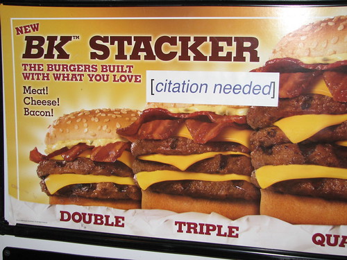 Panneau publicitaire représentant un burger. La publicité comporte un texte vantant les mérites du burger. Un autocollant avec le texte « citation needed » a été collé sur la publicité, à la suite du texte.