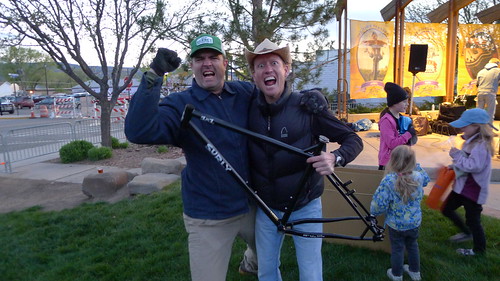 Front view of 2 people standing shoulder to shoulder, with one of them holding up a black Surly 1x1 bike frame