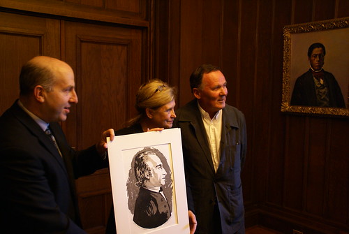 3 people hold a portrait while posing for a photo.