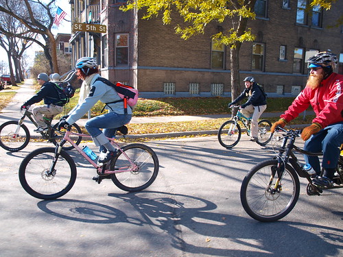 Left side view of cyclists, riding Surly bikes, down a city street, with buildings in the background