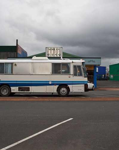 White RV with blue stripe parked in front of a Korean restaurant 