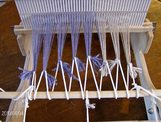 A cricket loom with the warp tied together in groups or “bouts” of threads with an overhand or lark’s head knot and secured to the apron bar with cord to minimize waste