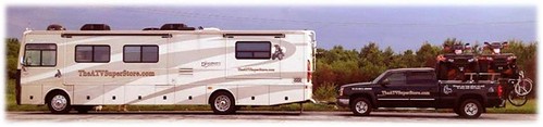 White RV towing a black truck with bikes and other gear in the bed