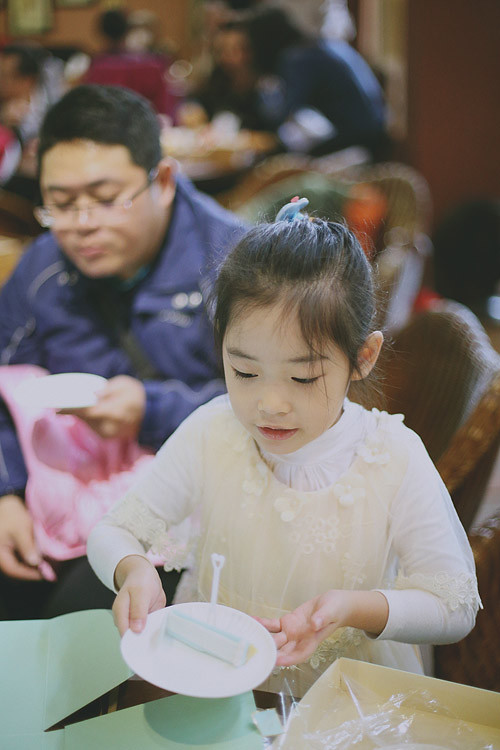 姐姐雙手端著一小塊生日蛋糕，爸爸坐在她身後。