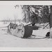 Man standing behind a loaded sled with a harnessed dog... / Homme debout derrière un traîneau chargé avec un chien...